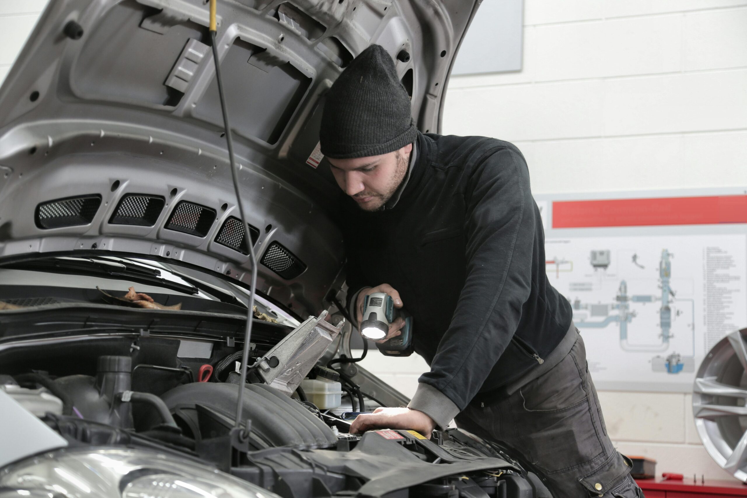 A mechanic closely inspects a car engine in a garage using a flashlight ensuring proper maintenance